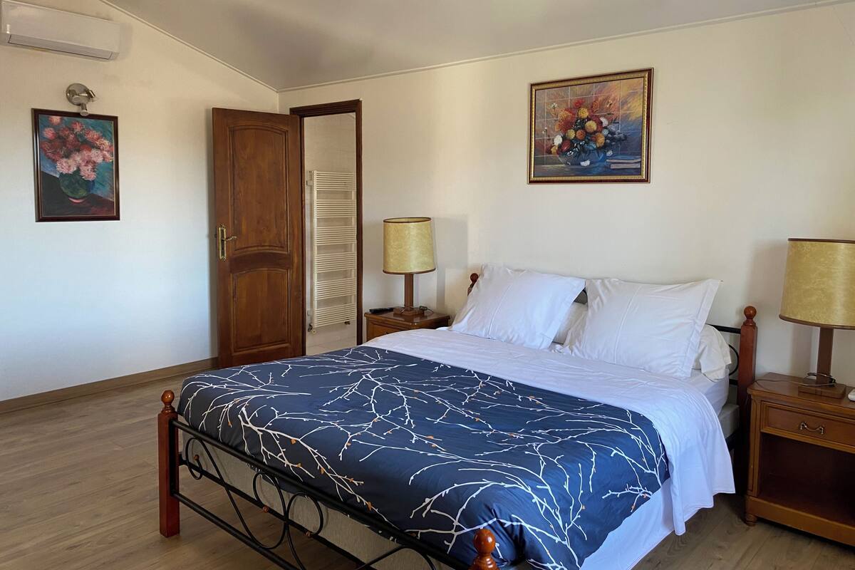 Un dormitorio con cama, dos mesitas de noche, un armario de madera, un radiador y dos lámparas de pared.