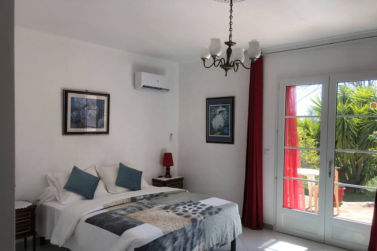 Un dormitorio con cama, mesita de noche, lámpara y ventana con cortinas.