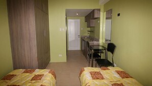 Ein Zimmer mit zwei Betten, einer Küchenzeile und einem durch eine offene Tür einsehbaren Badezimmer.