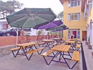 Des tables de pique-nique en plein air, dotées de parasols, un mur en pierre et un bâtiment avec une enseigne.
