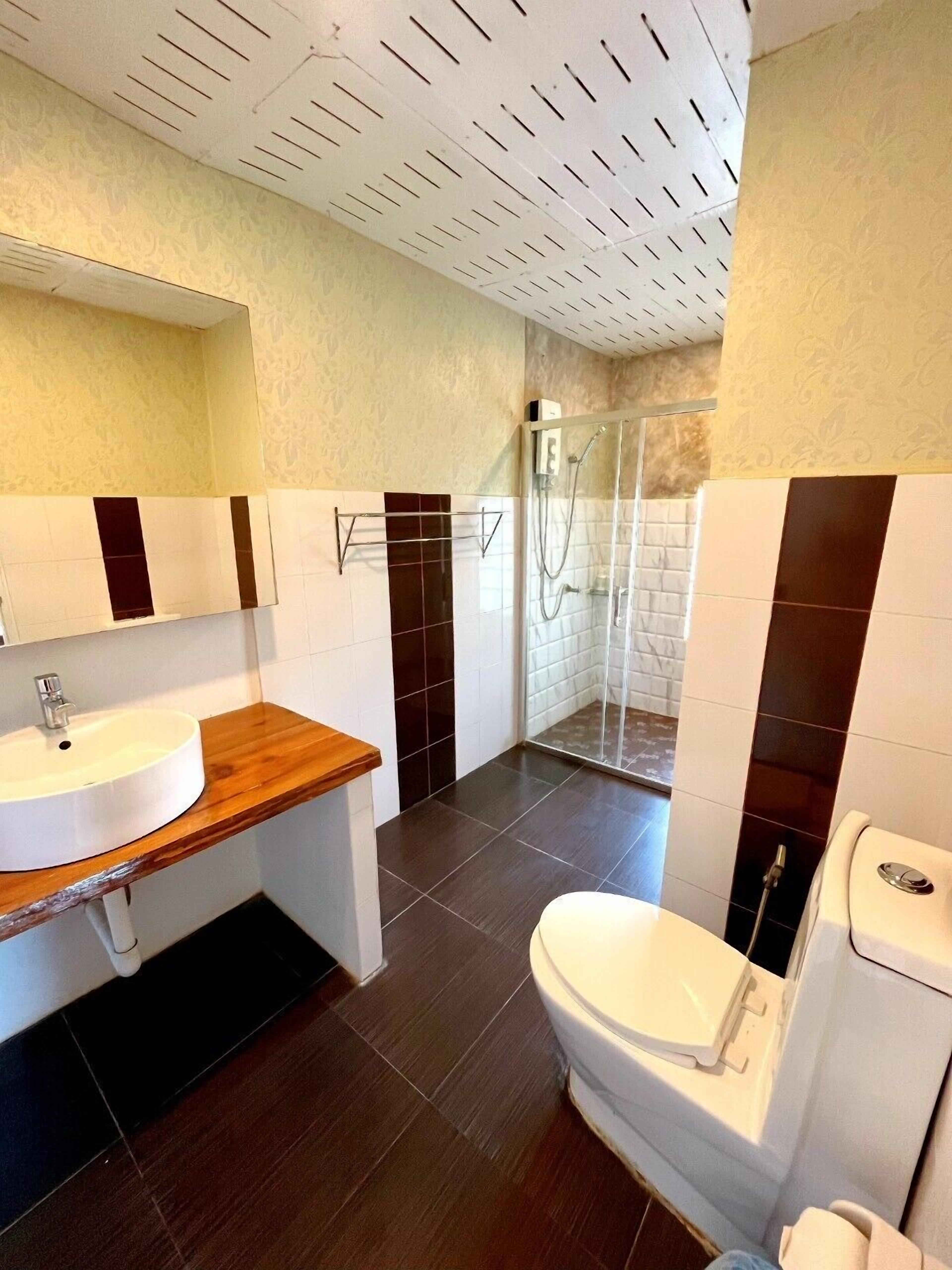 Une salle de bain moderne avec un meuble-lavabo en bois, un lavabo blanc, des toilettes et une douche séparée par une paroi en verre.
