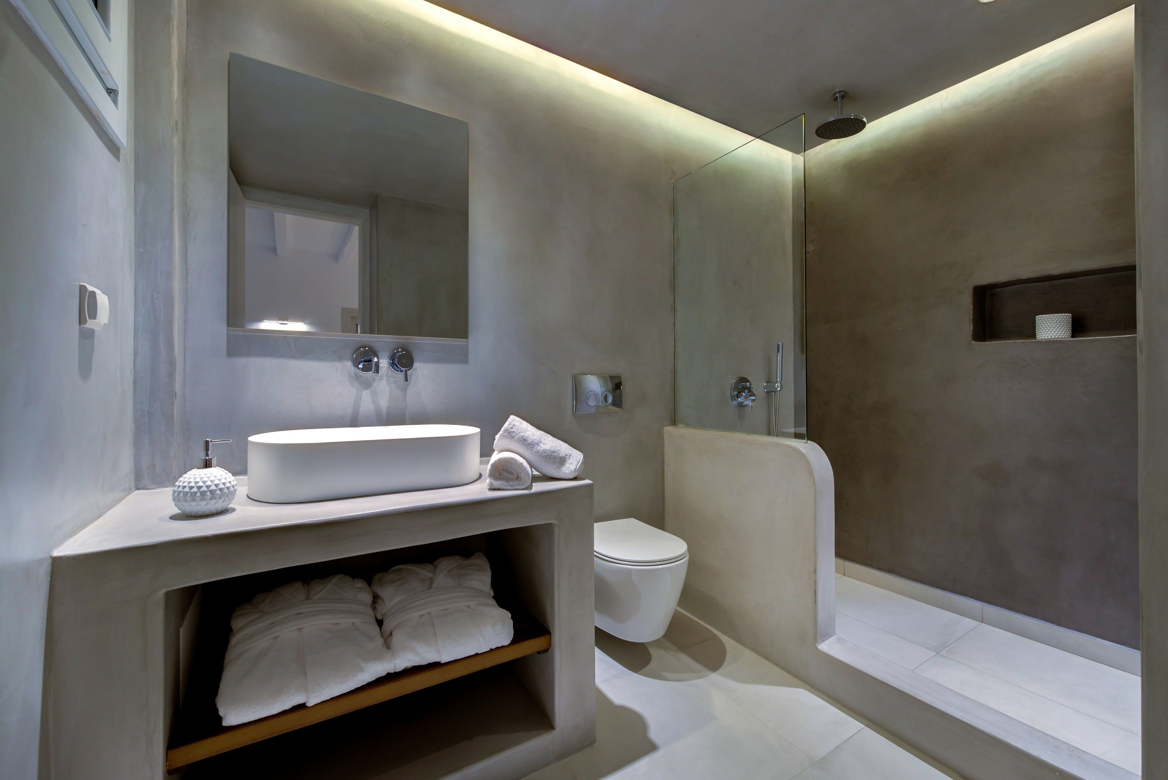 A modern bathroom with a large mirror, a round sink, a toilet, and a walk-in shower.