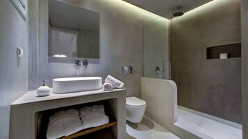 A modern bathroom with a large mirror, a round sink, a toilet, and a walk-in shower.