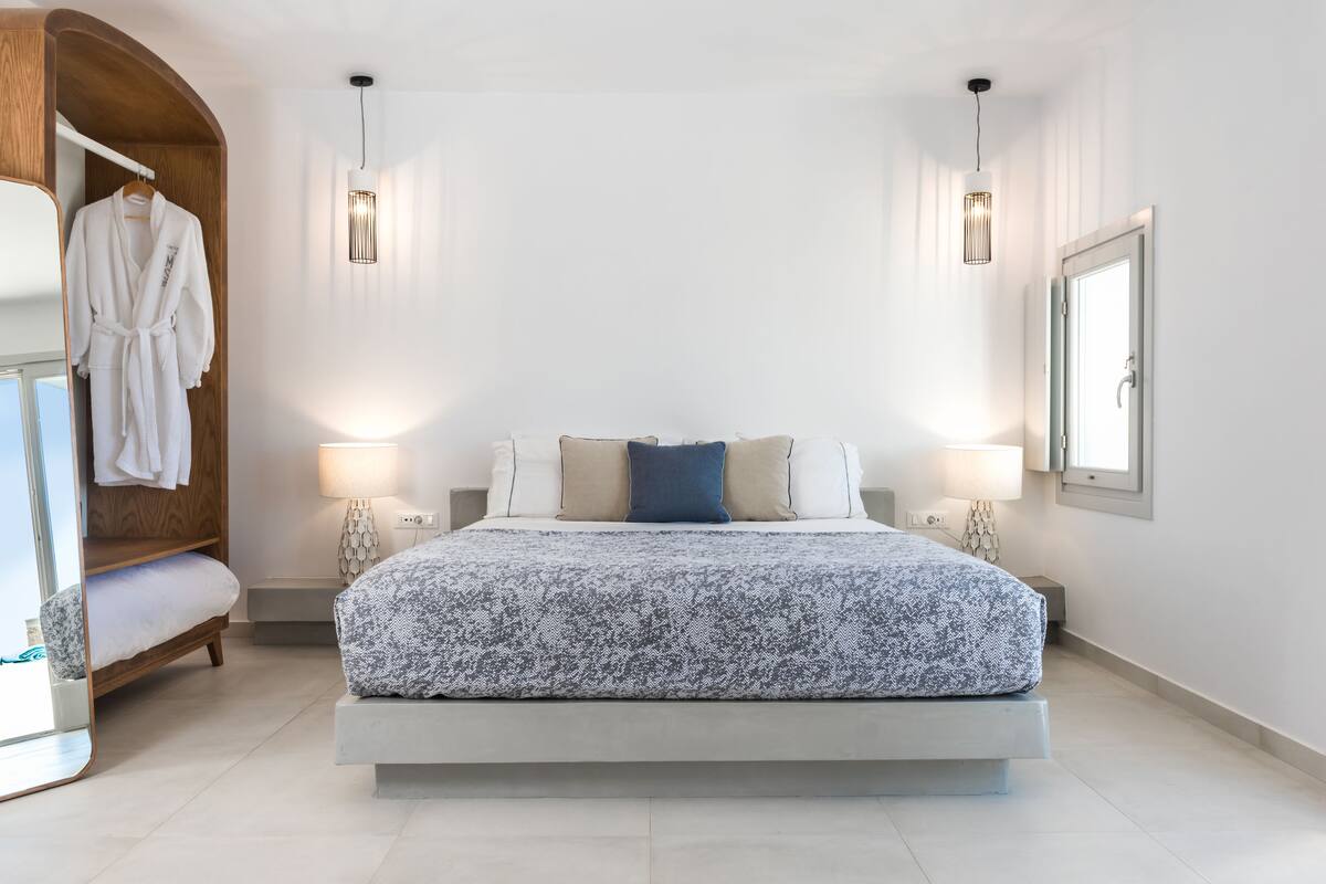 A modern bedroom with a large bed, bedside lamps, a wooden wardrobe, and a mirror.