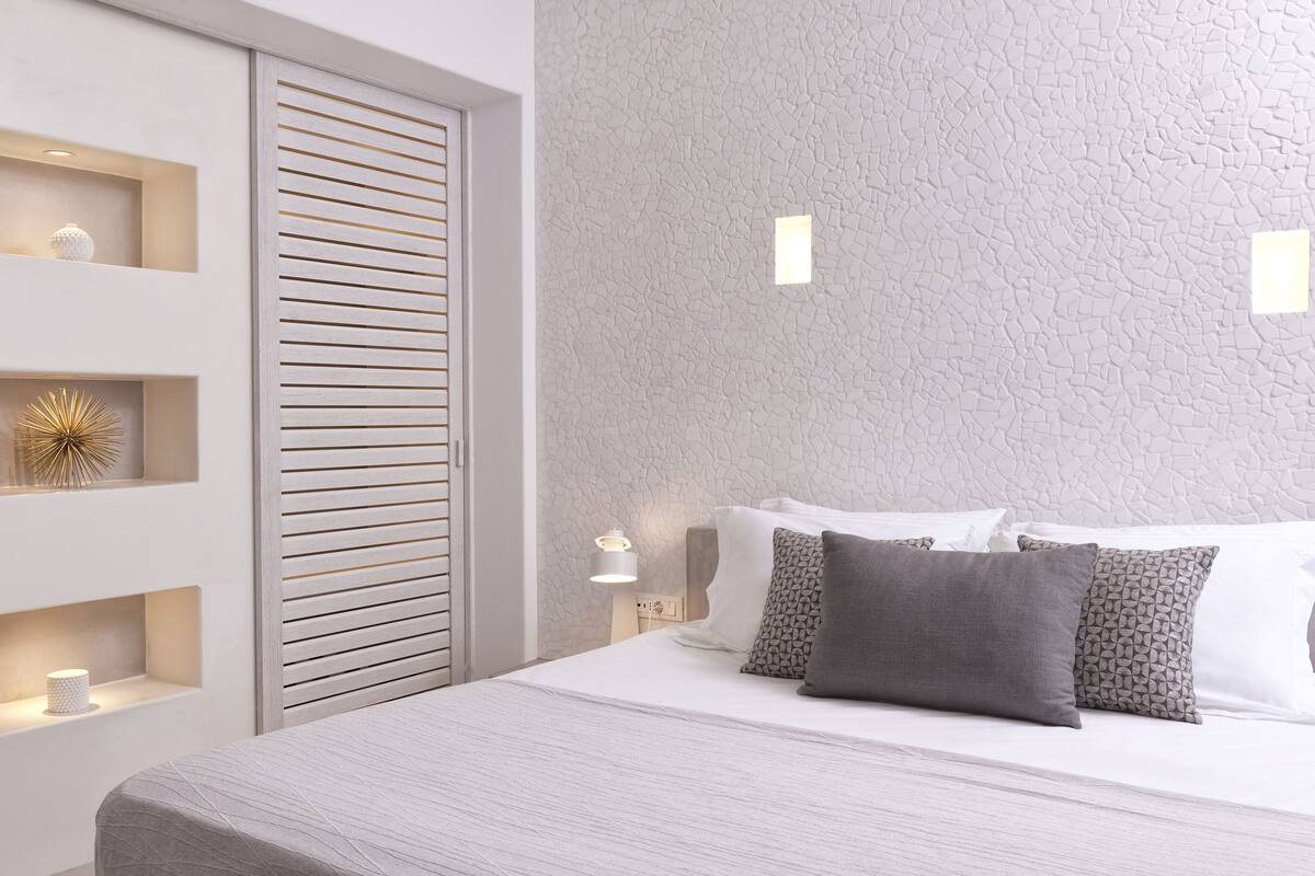 A bedroom with a bed, pillows, a nightstand, a wall-mounted light, and a textured wall.