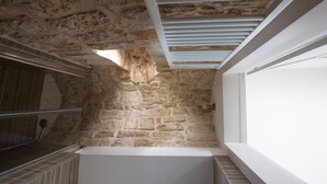 A stone-walled bathroom with a bathtub, a window, and a shower area. - Masseria Poli (Conversano)