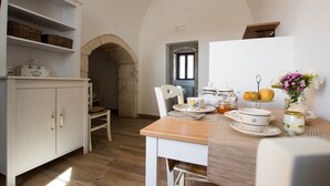 A dining area with a wooden table, white chairs, and a white cabinet with shelves. - Masseria Poli (Conversano)