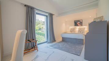 Un dormitorio moderno con un ventanal grande, una cama con cabecera gris, un sofá gris y un armario gris.