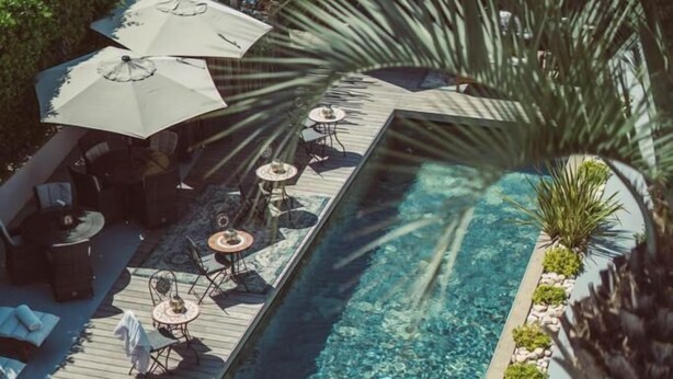 A rooftop pool area with lounge chairs, umbrellas, and a wooden deck. - Hotel Le Mandala (Saint-Tropez)