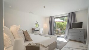 A modern hotel room with a large bed, a television, a desk, and a view of the outdoors. - Hotel Le Mandala (Saint-Tropez)