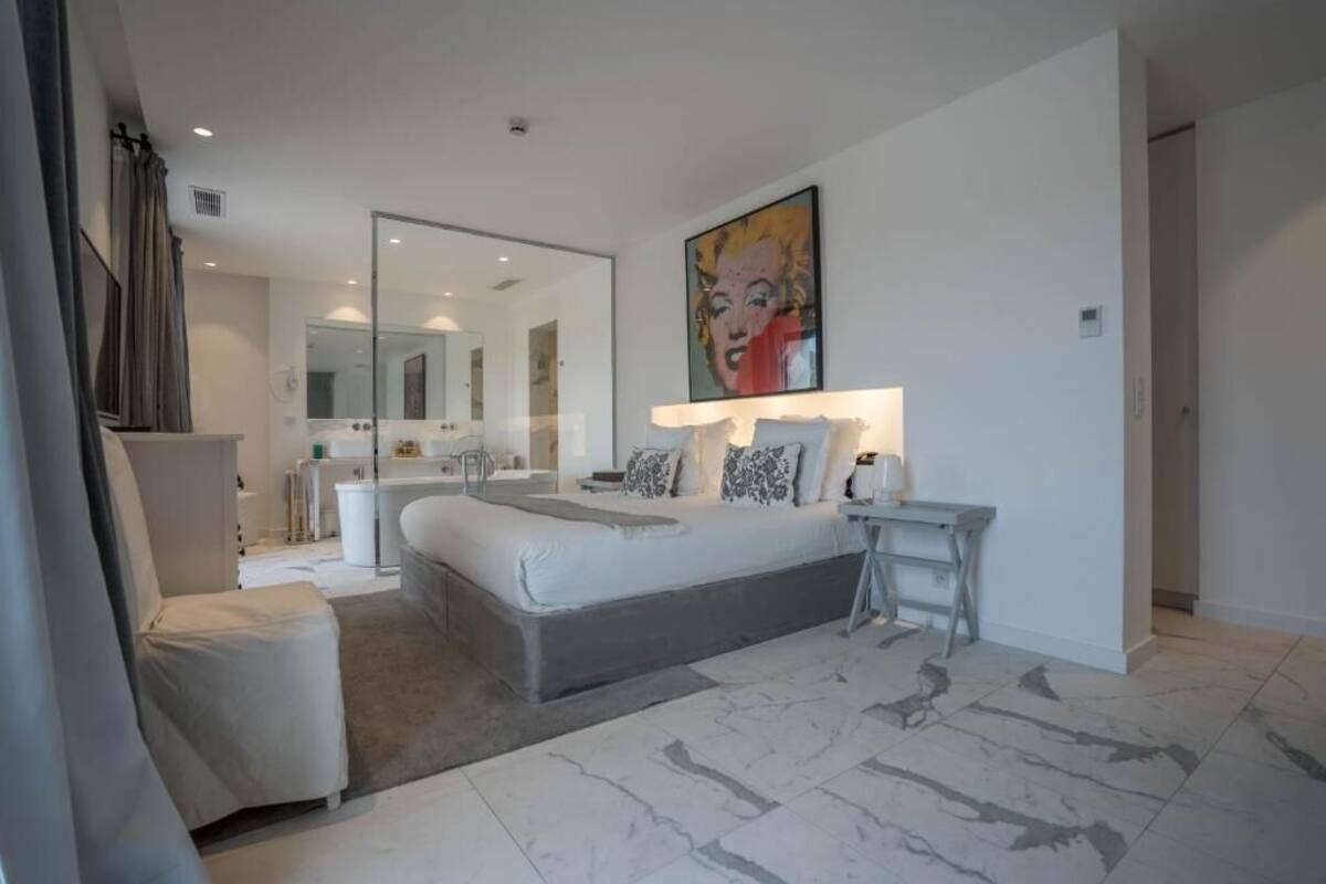 Un dormitorio moderno con una cama grande, una mesita de noche, una silla, un espejo y un cuadro en la pared.