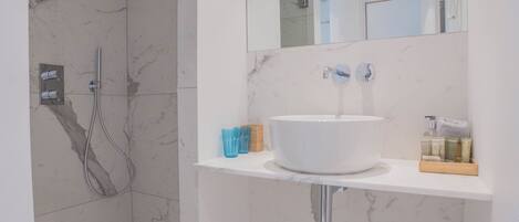 A modern bathroom with a white sink, marble walls, and a shower area.