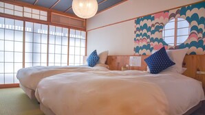 A traditional Japanese-style room with tatami flooring, two beds with white bedding and blue pillows, a shoji screen door, and a colorful wave-patterned wall. - Chika Seiryu (Kyoto)