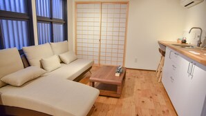 A modern living room with a sofa, a coffee table, and a kitchen area with a sink and cabinets. - Chika Seiryu (Kyoto)