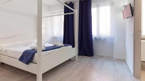 Een moderne hotelkamer met een hemelbed, een flatscreen televisie aan de muur en een groot raam met gordijnen.
