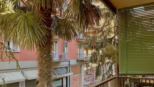 Een balkon met uitzicht op een roze gebouw, een palmboom en een gesloten winkel.