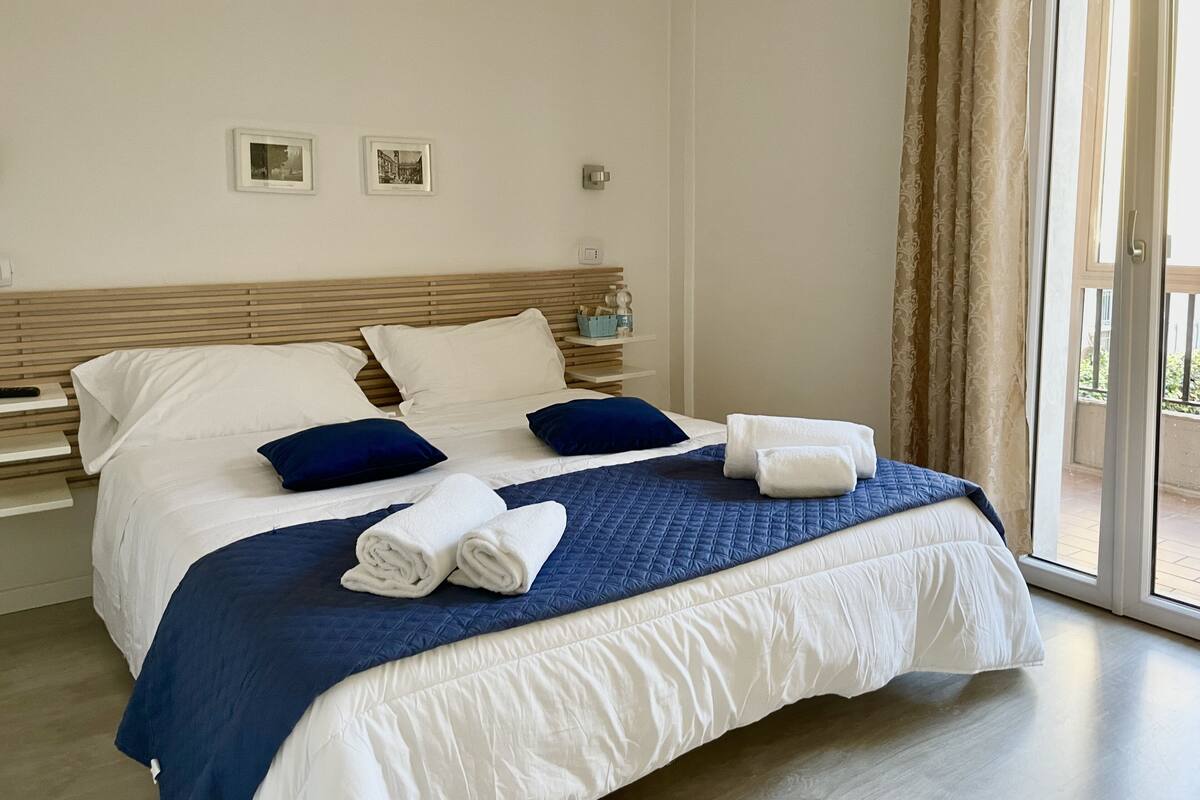 Une chambre d’hôtel avec un lit, des oreillers, une table de chevet et une fenêtre avec des rideaux.