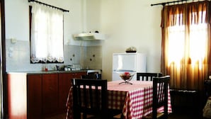 Une petite cuisine avec une table à manger pour deux personnes, un réfrigérateur et une fenêtre avec des rideaux.