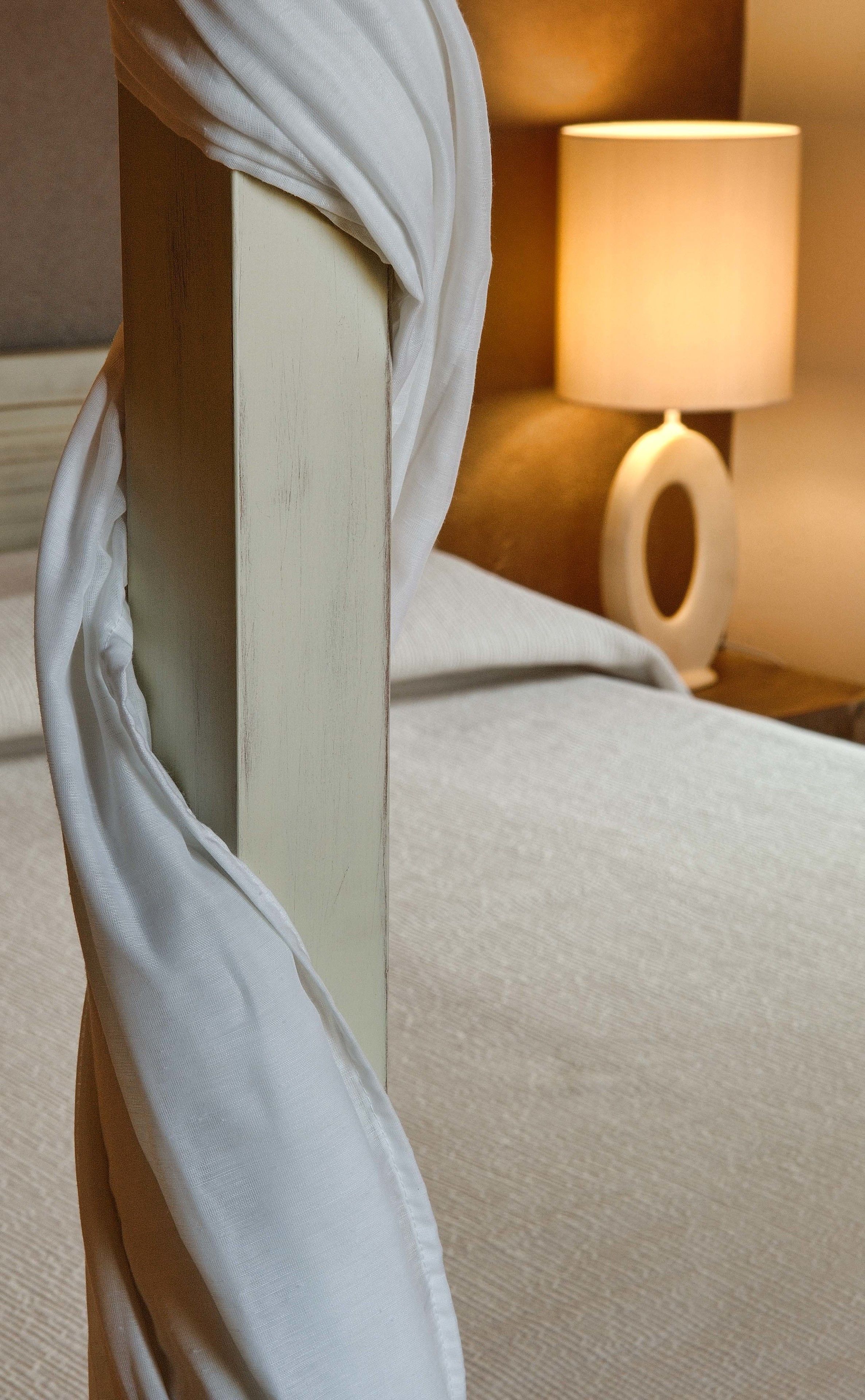 Un gros plan d’un tissu blanc drapé sur une structure en bois, peut-être un meuble, avec une lampe à lumière douce en arrière-plan.