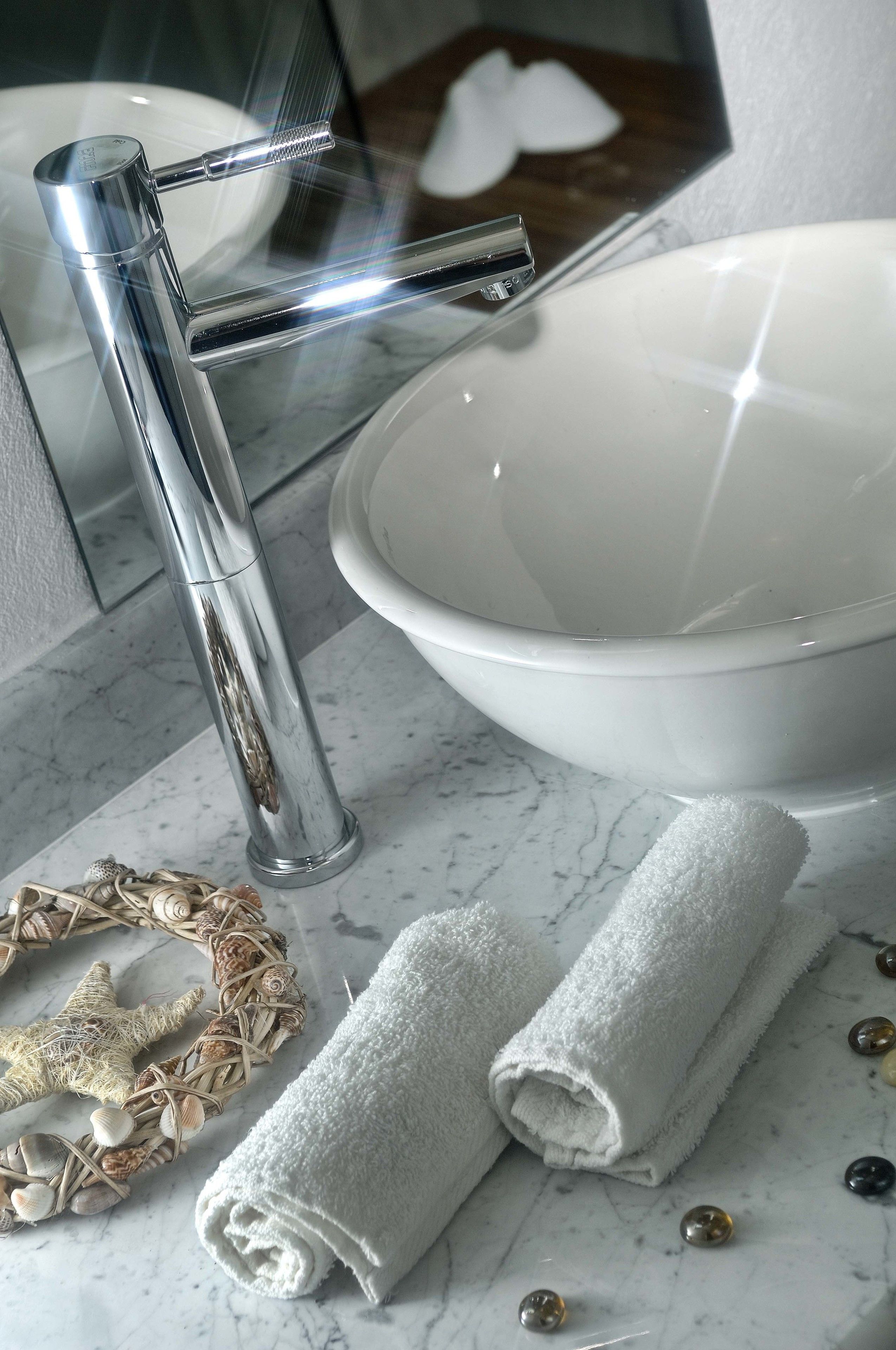 A bathroom with a white sink, chrome faucet, and a decorative starfish and seashell arrangement.
