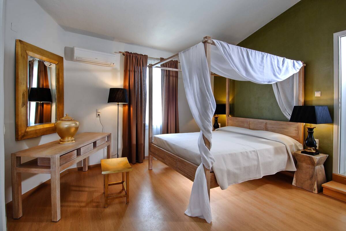 Ein Schlafzimmer mit einem Himmelbett, einem Holztisch mit Lampe und einem Nachttisch ebenfalls mit Lampe.
