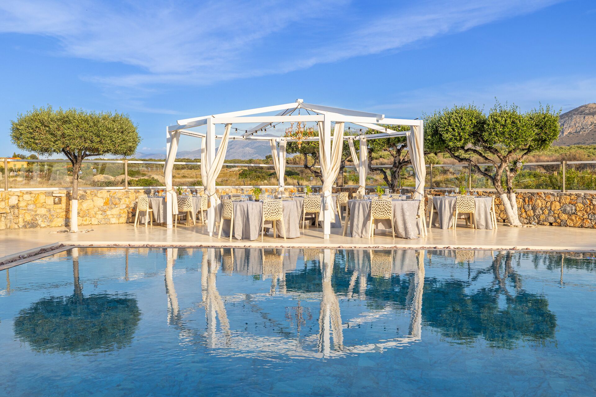 Zona de piscina con pérgola, paredes de piedra y mesas dispuestas para comer.