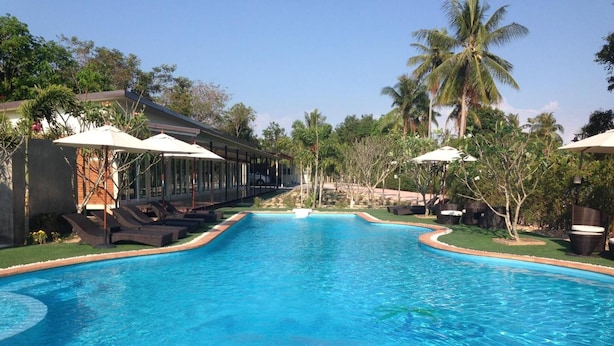 A swimming pool with lounge chairs and umbrellas, surrounded by palm trees and greenery. - Check In & Chill Out Laem Sok Pier (Trat)