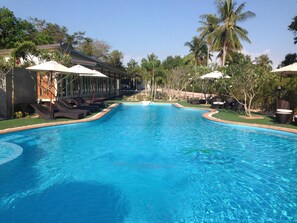 A swimming pool with lounge chairs and umbrellas, surrounded by palm trees and greenery. - Check In & Chill Out Laem Sok Pier (Trat)