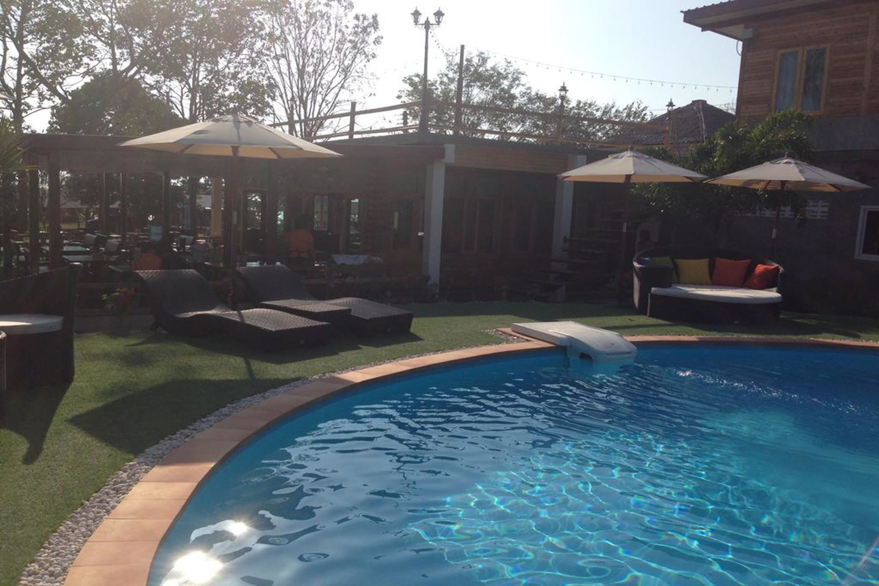A backyard with a swimming pool, outdoor seating, and umbrellas.