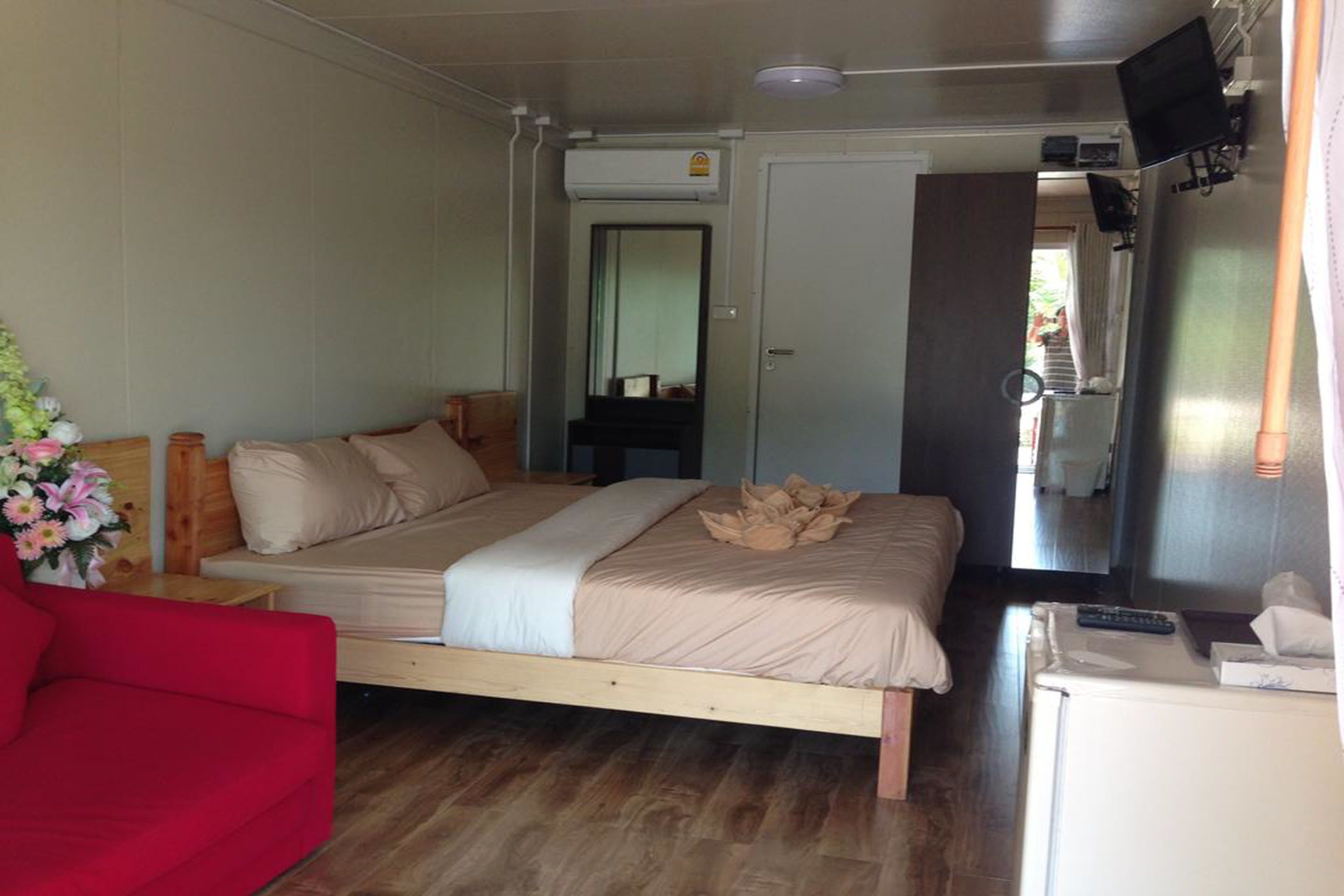 A bedroom with a bed, a red chair, a small table, a TV, and a refrigerator.