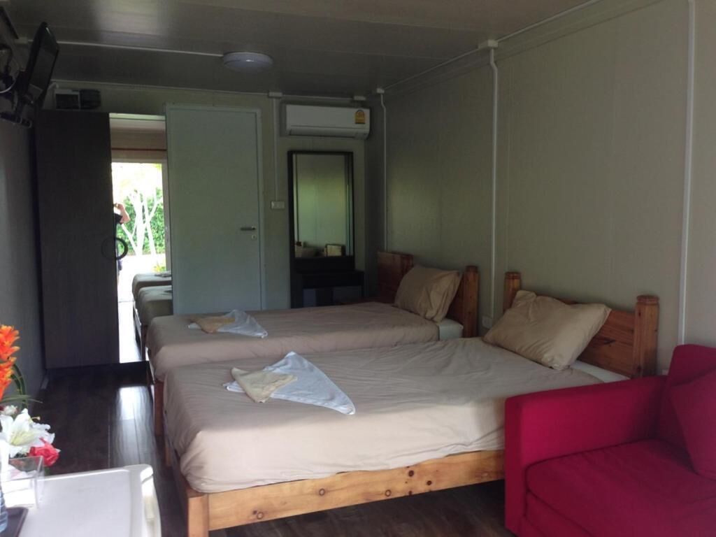 A room with two beds, a red chair, and a desk with a vase of flowers.