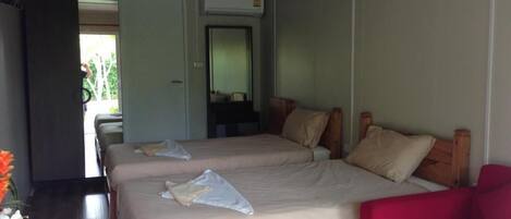 A room with two beds, a red chair, and a desk with a vase of flowers.