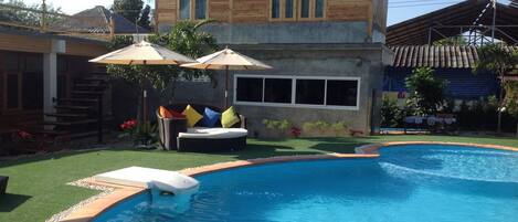 A swimming pool with a wooden house in the background.