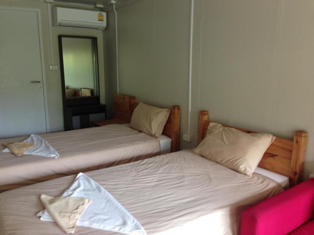 Deux lits simples avec des têtes de lit en bois, un miroir et une porte blanche.