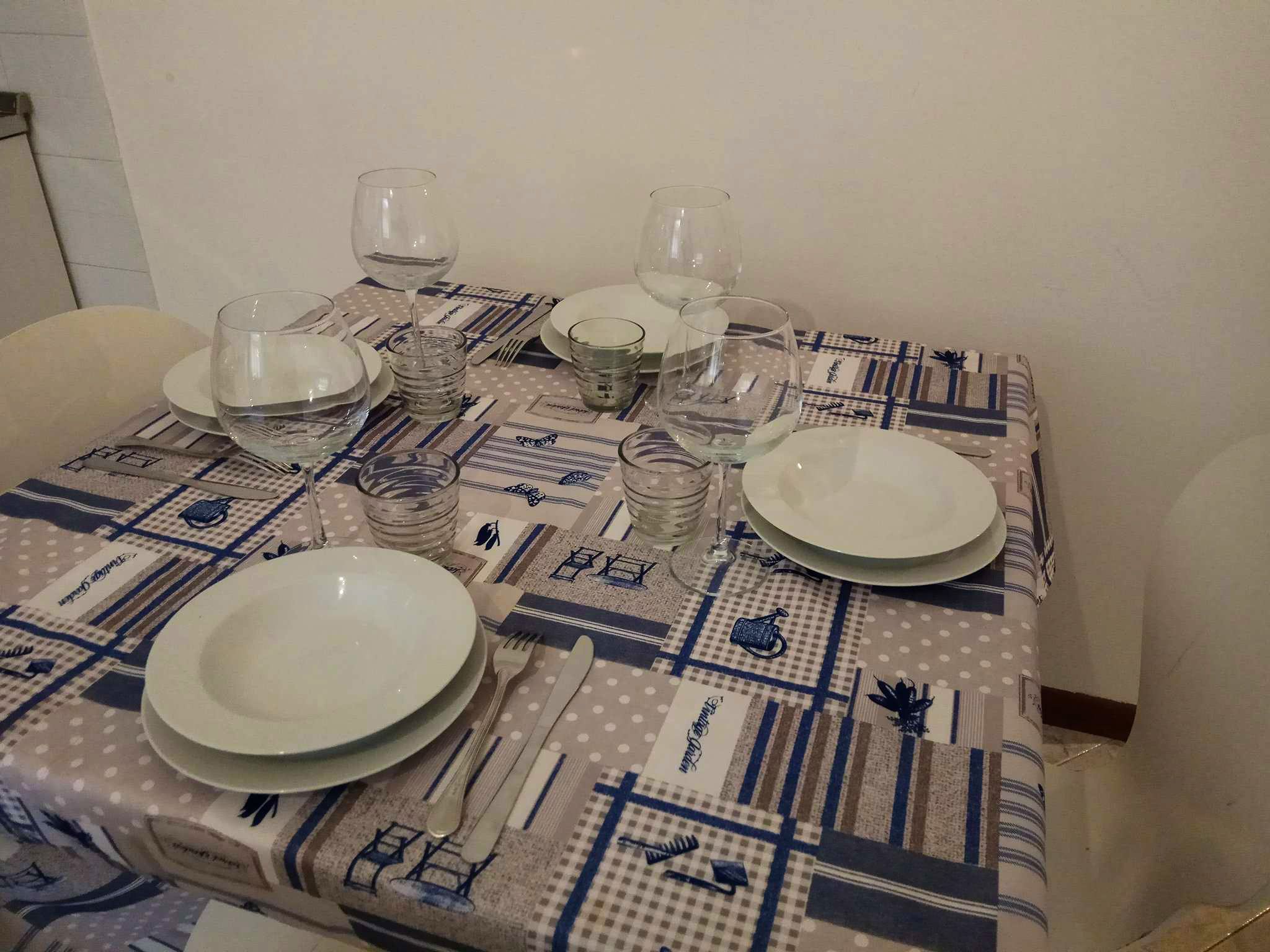 Una mesa de comedor dispuesta con platos, vasos y cubiertos, cubierta por un mantel estampado.