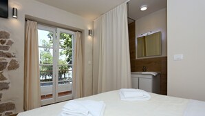 Een hotelkamer met een bed, twee handdoeken, een raam met gordijnen, een badkamer met een spiegel en uitzicht op bomen.