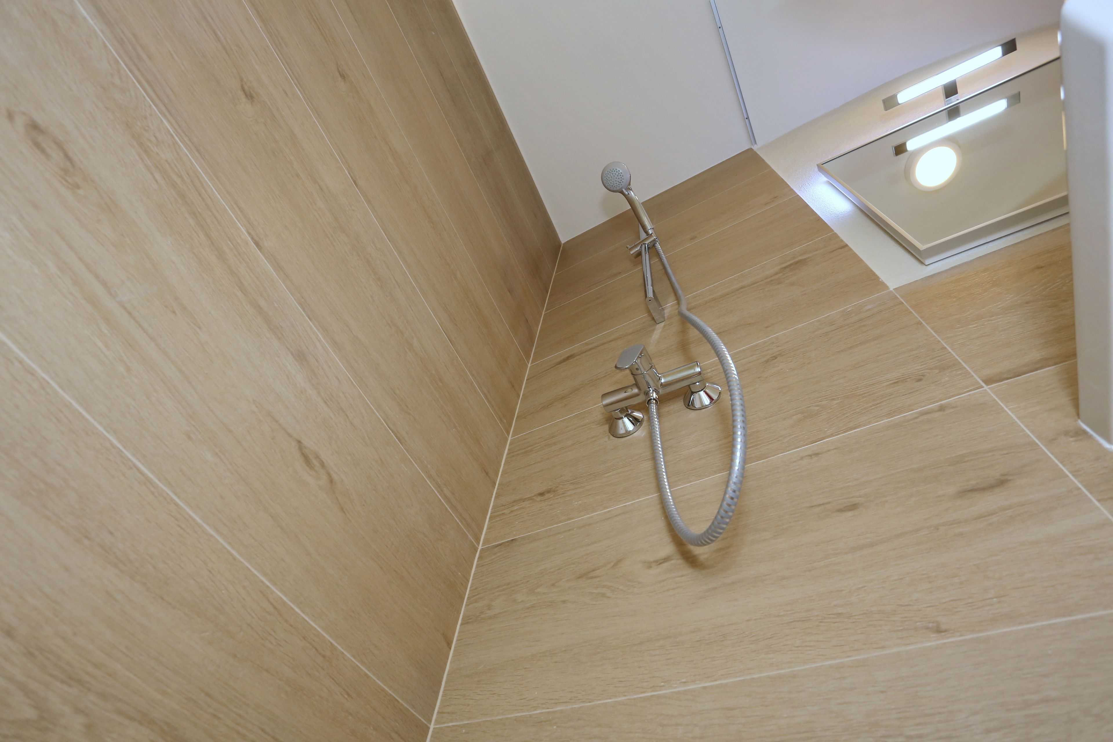 A shower area with wooden flooring and a modern showerhead.