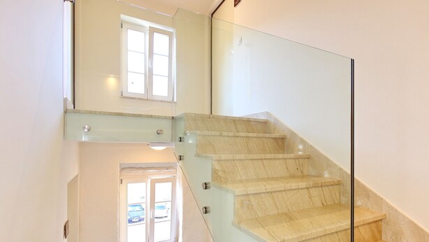 Een moderne trap met glazen balustrades en een stenen muur aan de onderkant.