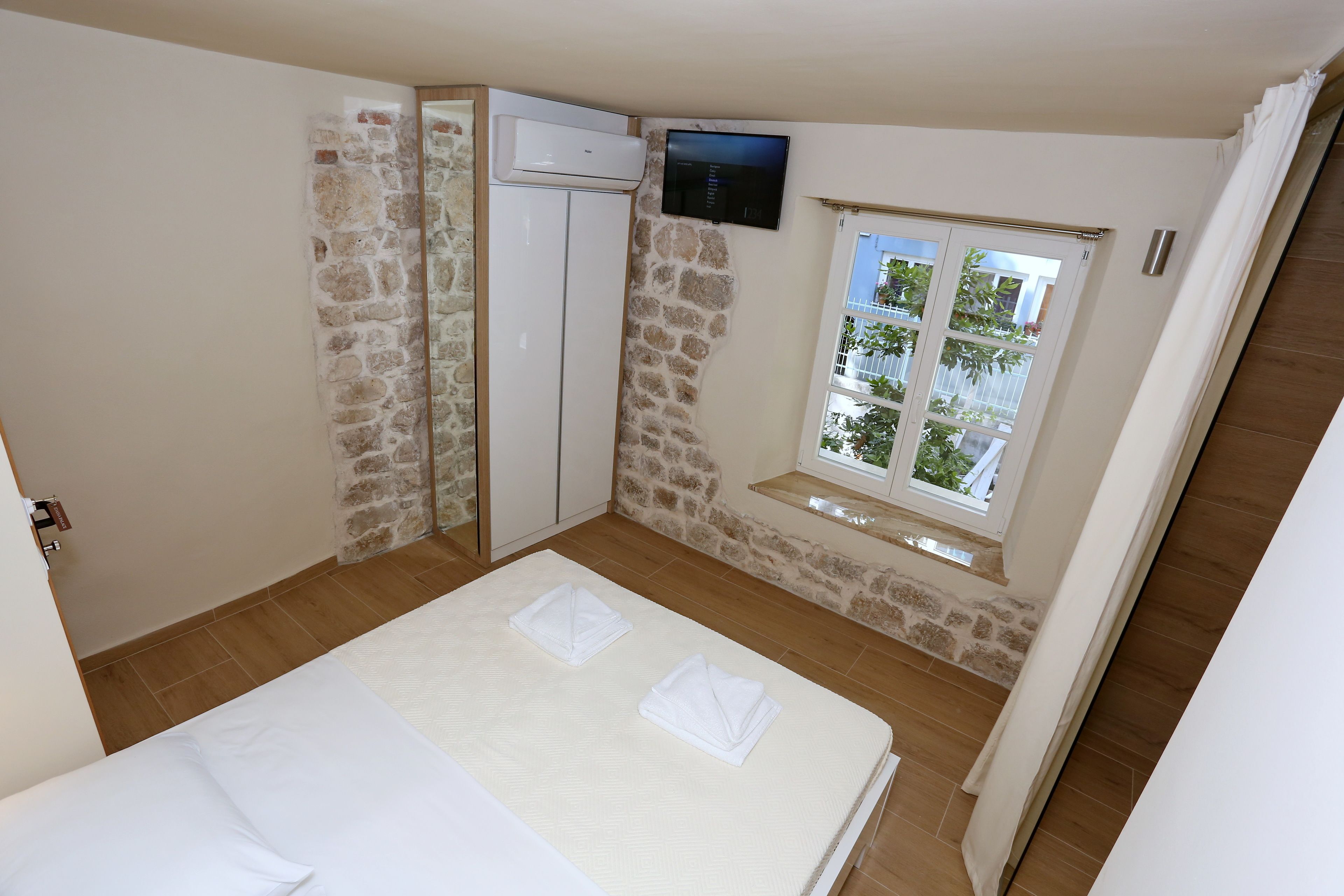 A bedroom with a stone wall, a TV mounted above a window, and a bed with towels.