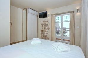 A hotel room with a bed, a TV mounted on the wall, a stone accent wall, and a balcony with curtains. - Idassa Palace (Zadar)