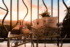 A balcony with a metal railing, a small table with a vase of flowers, a teapot, and a coffee pot.