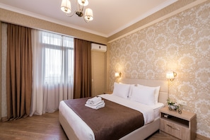 A hotel room with a large bed, a nightstand with a lamp, and a window with curtains.