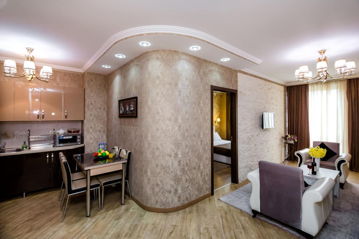 A modern hotel room with a kitchen area, a dining table, and a living area with a sofa and armchairs.