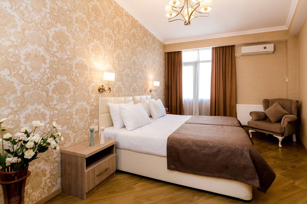 A hotel room with a large bed, bedside tables, a chair, and a window with curtains.