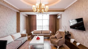 A modern living room with a chandelier, sofas, a coffee table, and a flat-screen TV. - Dat Exx Apartments (Tbilisi)