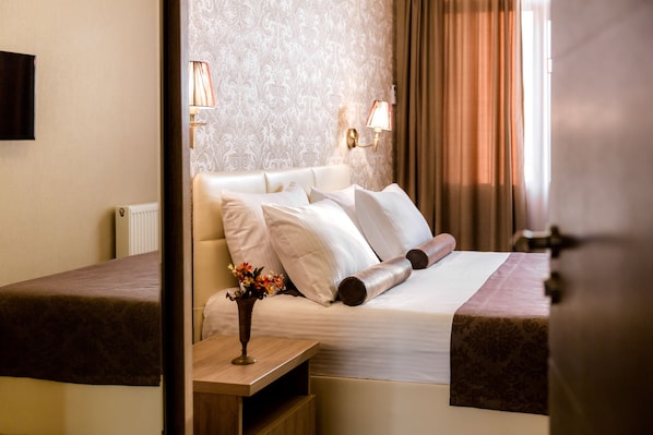 A hotel room with a large bed, a bedside table with a vase of flowers, and a wall-mounted lamp.