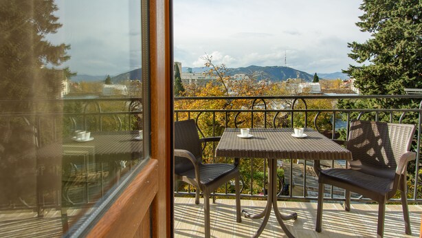A balcony with a table and chairs, overlooking a cityscape with mountains in the distance. - Dat Exx Apartments (Tbilisi)