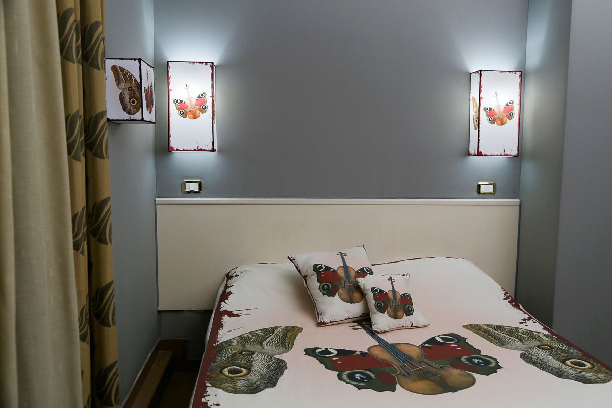 A bedroom with a bed featuring butterfly and bird designs, two wall-mounted light fixtures, and a curtain with a leaf pattern.