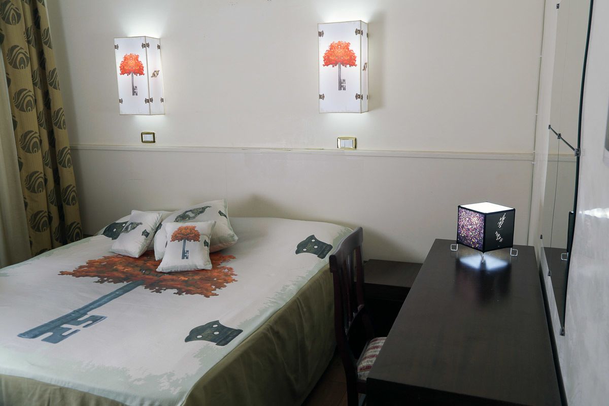 A hotel room with a bed, pillows, a nightstand, and wall-mounted lights.