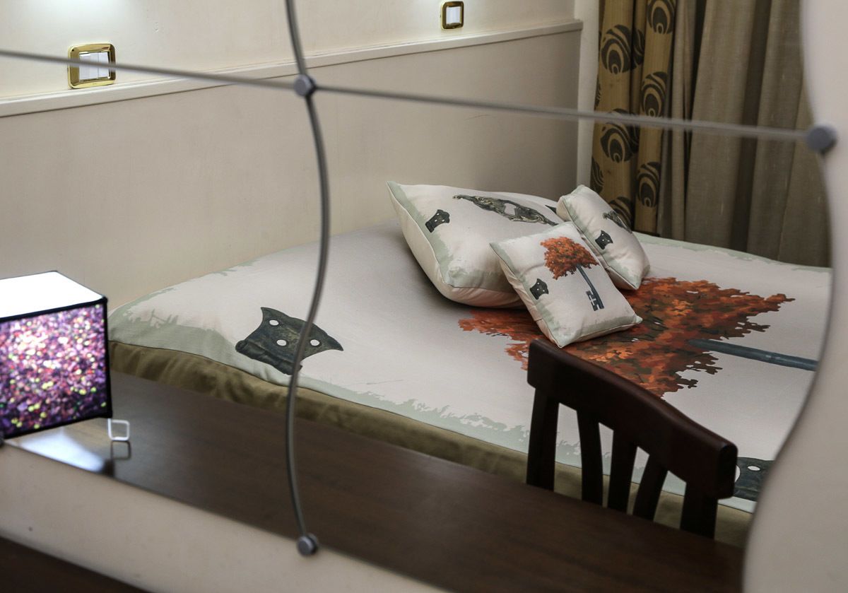 Una cama bien hecha con almohadas estampadas, una mesita de noche con lámpara y una silla.